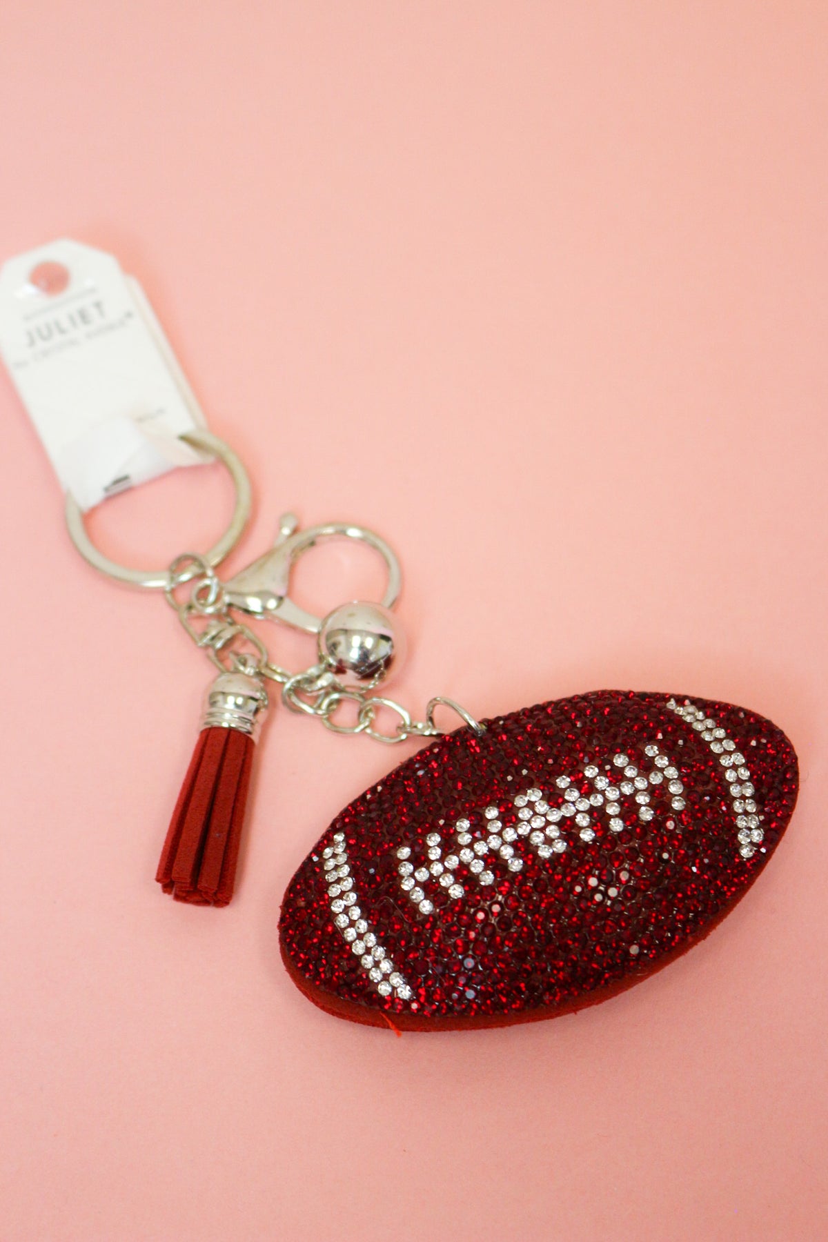 Close-up of red rhinestone football keychain with clear stone laces, red tassel and silver-tone clasp on pink.