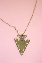 Close-up of antiqued gold-tone arrowhead pendant with scattered round iridescent jewel accents on a fine-link chain.
