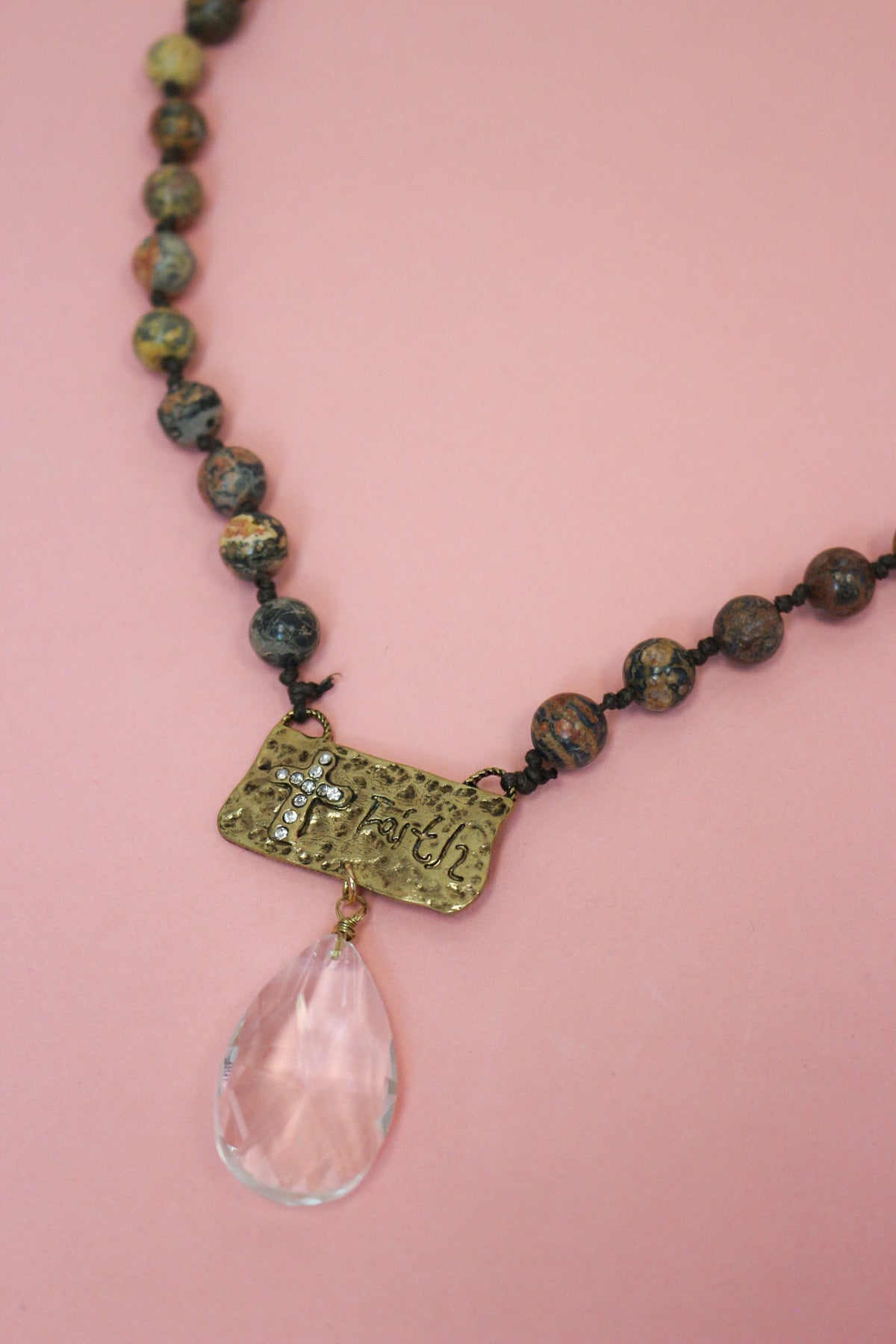 Close-up of brown beaded necklace with antiqued gold-tone faith plaque, sparkling cross, and clear faceted teardrop.
