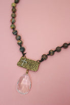 Close-up of brown beaded necklace with antiqued gold-tone faith plaque, sparkling cross, and clear faceted teardrop.