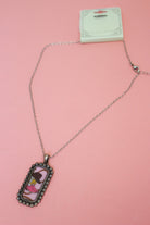 Western Boot Tag Necklace with silver-tone chain, illustrated rectangular pendant, lobster clasp, and extender on pink.