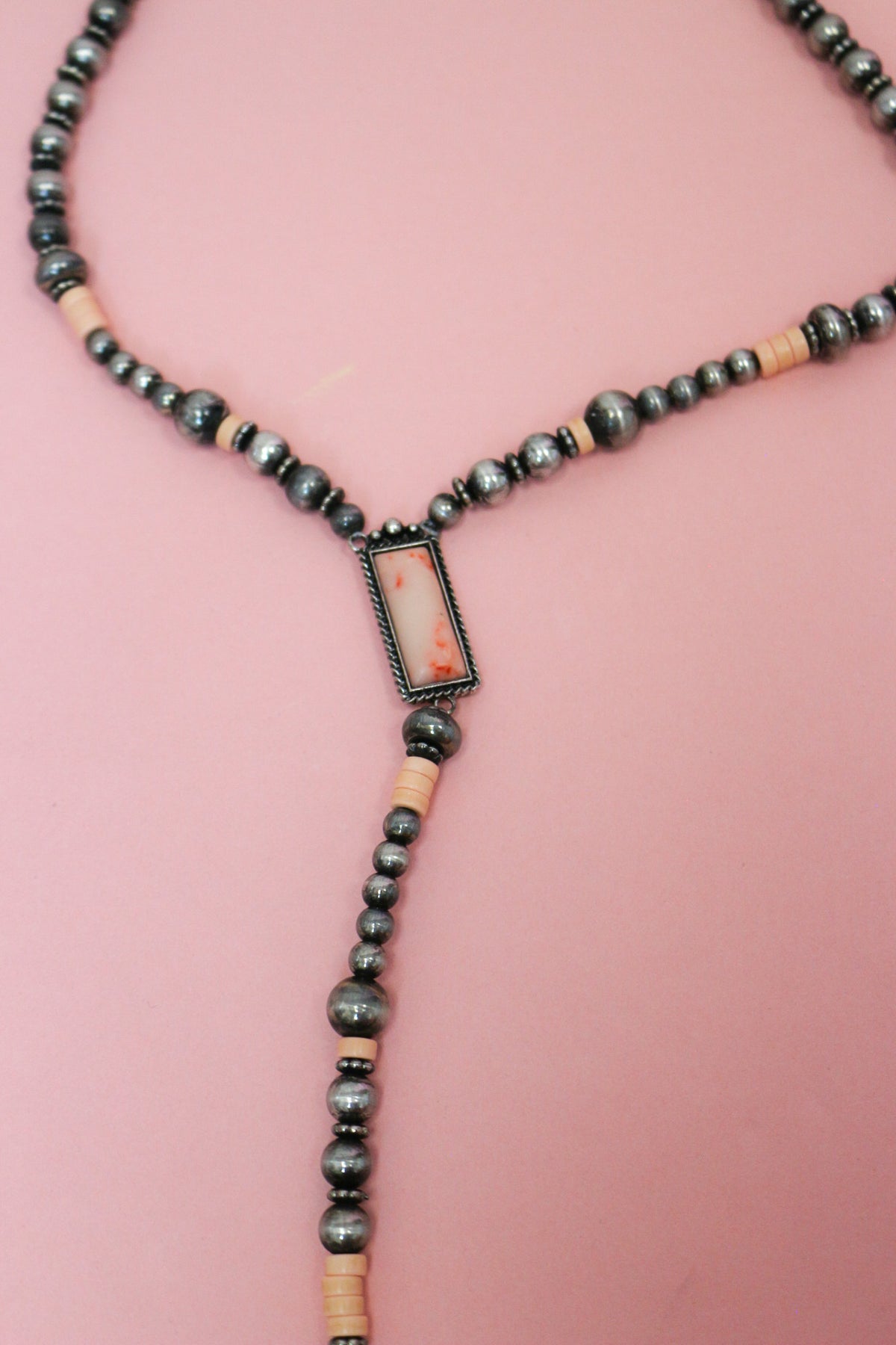 Close-up of silver-tone and pale pink beaded Y necklace with a framed rectangular pink centerpiece and long beaded drop.