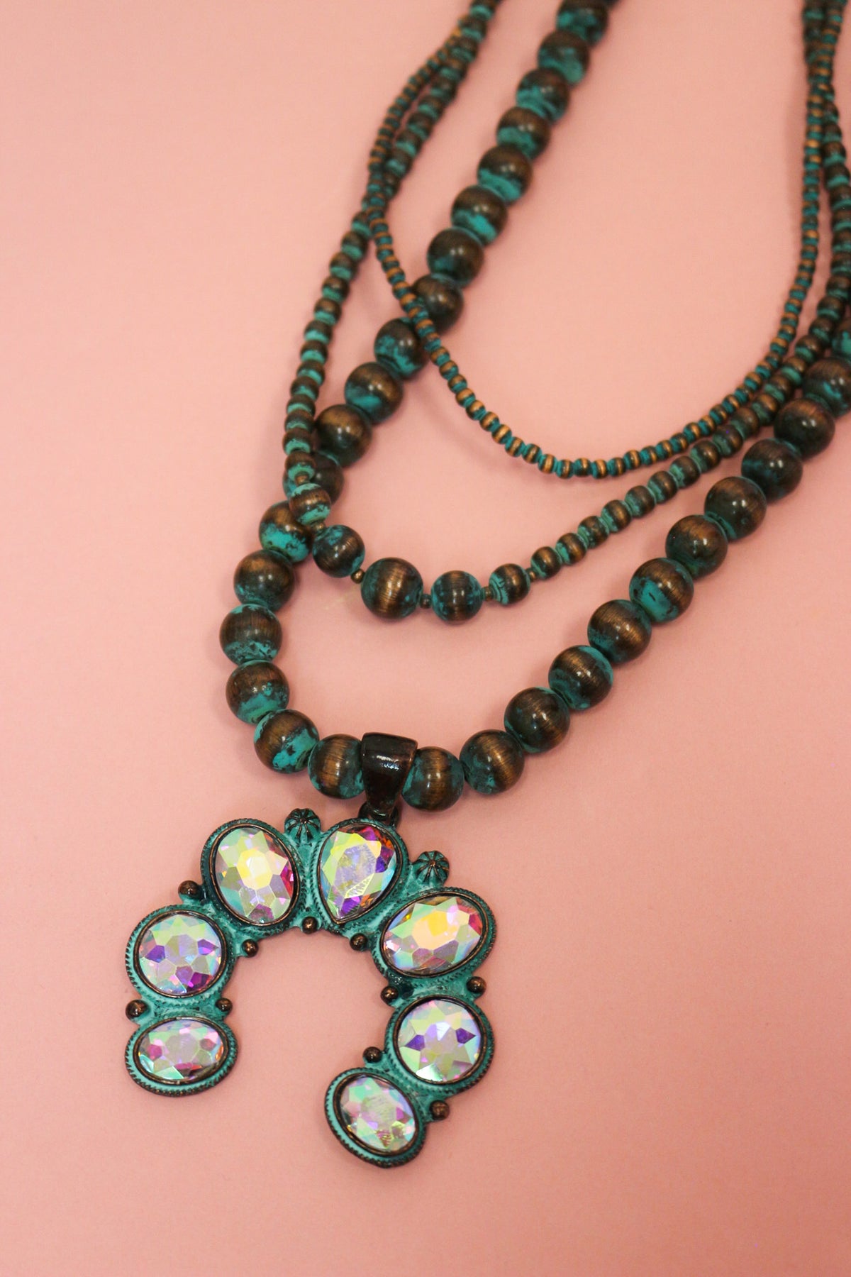 Close-up of layered Western necklace with turquoise-colored beads and a crescent pendant with iridescent faceted accents.