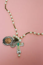 Close-up of pearl-look Western necklace with penny charm, textured cross pendant and turquoise-colored accent on pink.