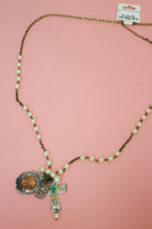 Pearl-look beaded chain Western necklace with penny charm and layered cross pendant laid out on a pink background.