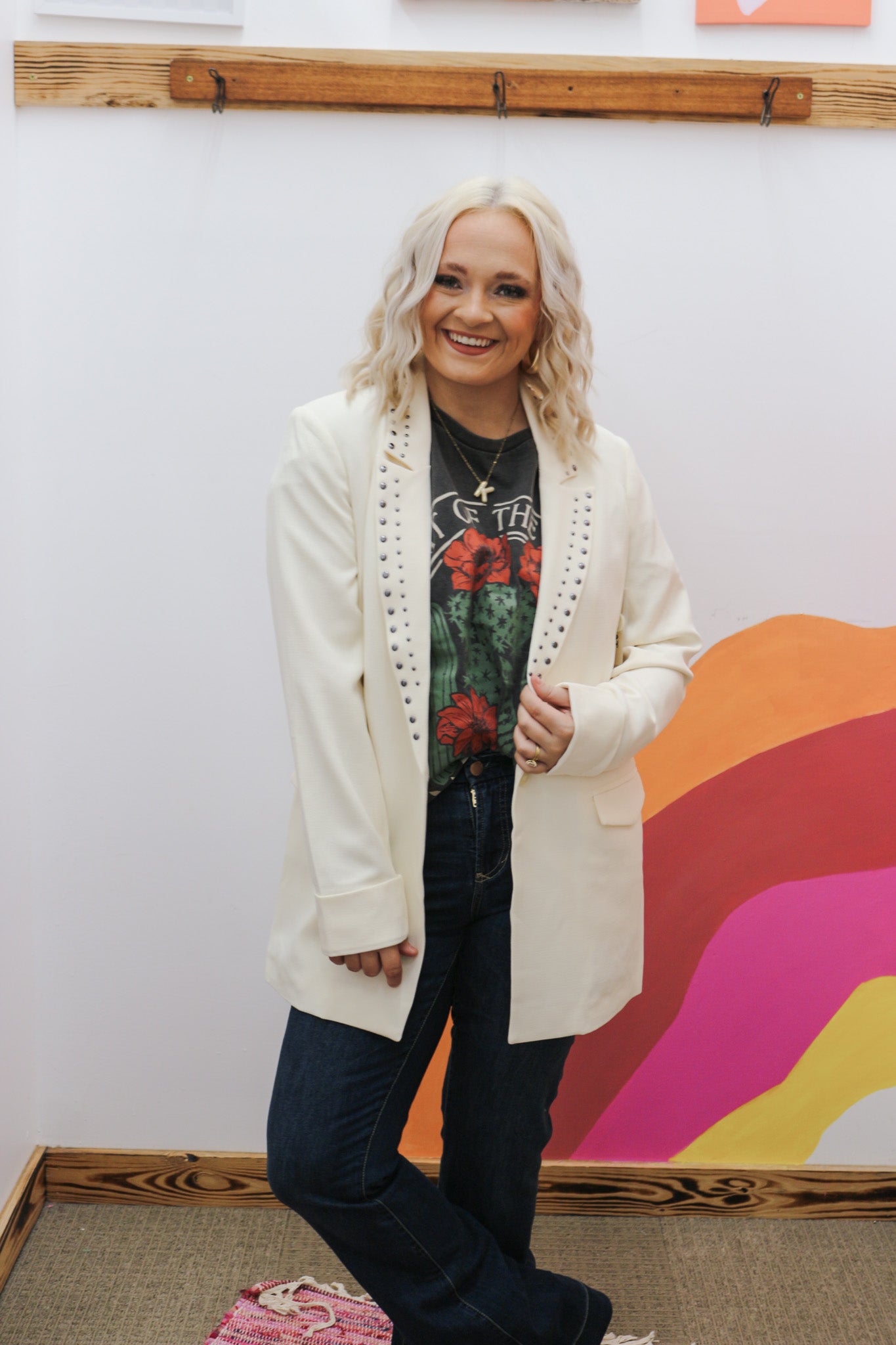 Person wearing a white cardigan over a graphic t-shirt with a colorful abstract painting in the background.