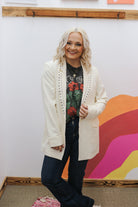 Person wearing a white cardigan over a graphic t-shirt with a colorful abstract painting in the background.