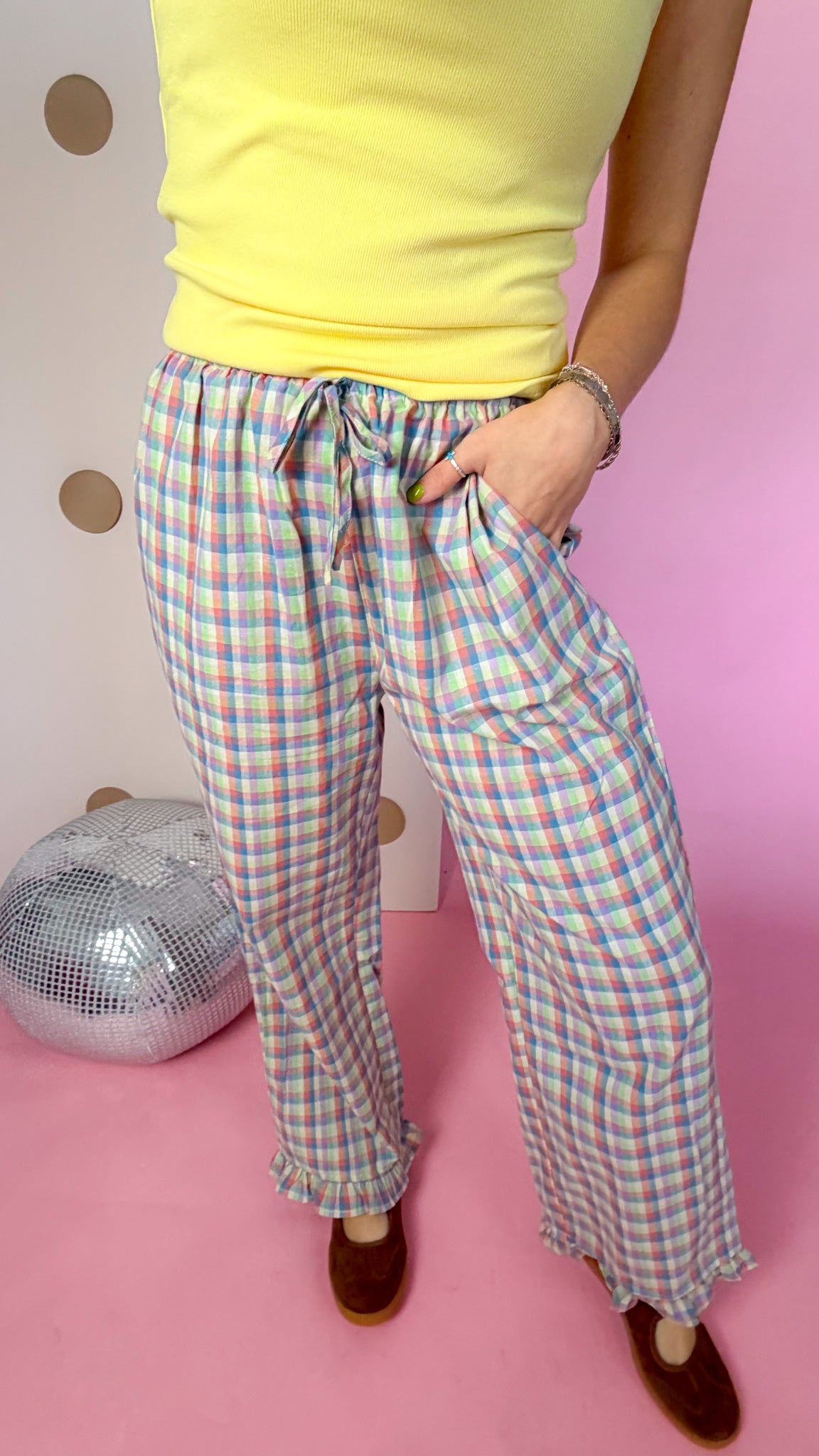 Close-up of plaid pants showing the tie waist, front patch pocket, wide legs, and ruffle hems