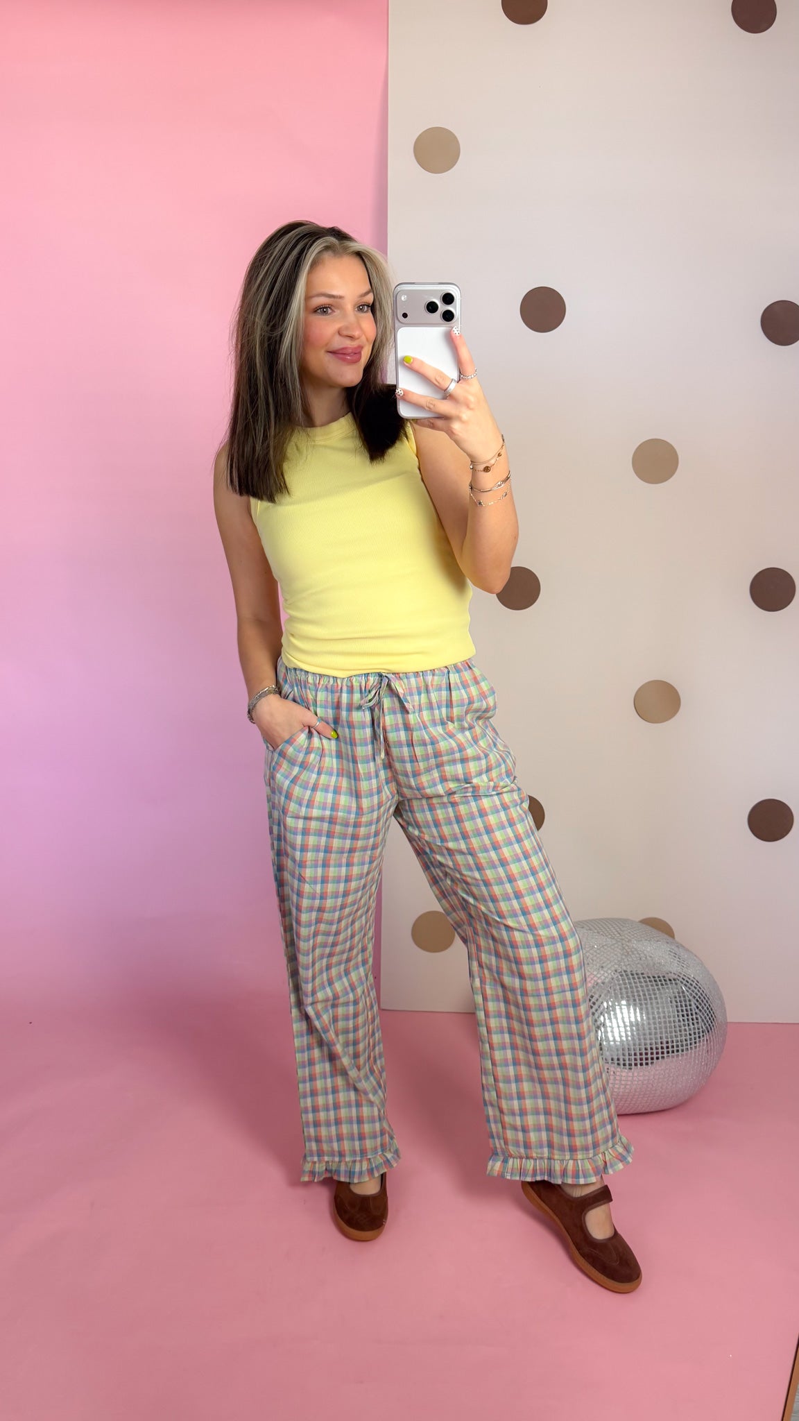 Mirror selfie showing Daisy yellow ribbed tank top styled with plaid wide-leg pants and brown flats.