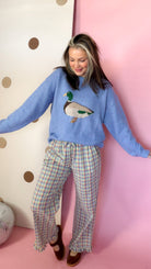 Women's coral and blue plaid ruffle pants paired with a blue duck sweater, showing the wide-leg silhouette