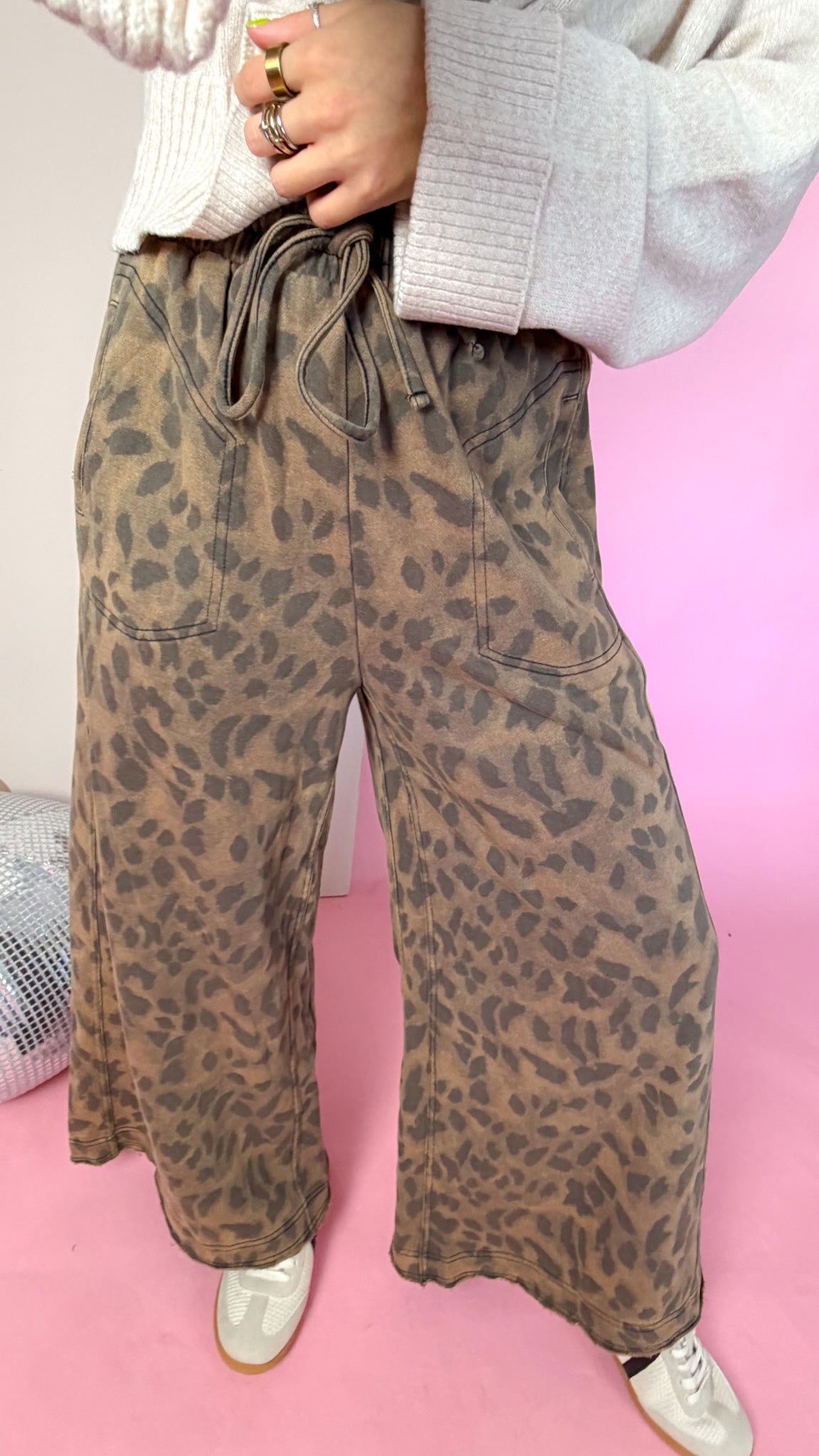 Close-up of mocha leopard pants showing the tie elastic waistband, front pockets and wide legs.