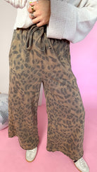 Close-up of mocha leopard pants showing the tie elastic waistband, front pockets and wide legs.