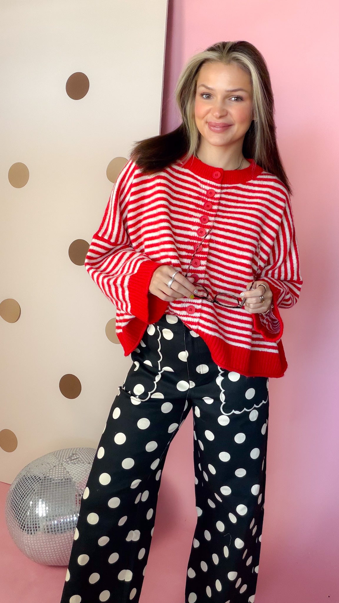 Front view of women's red and ivory striped button sweater with red trim, styled with black polka-dot pants.