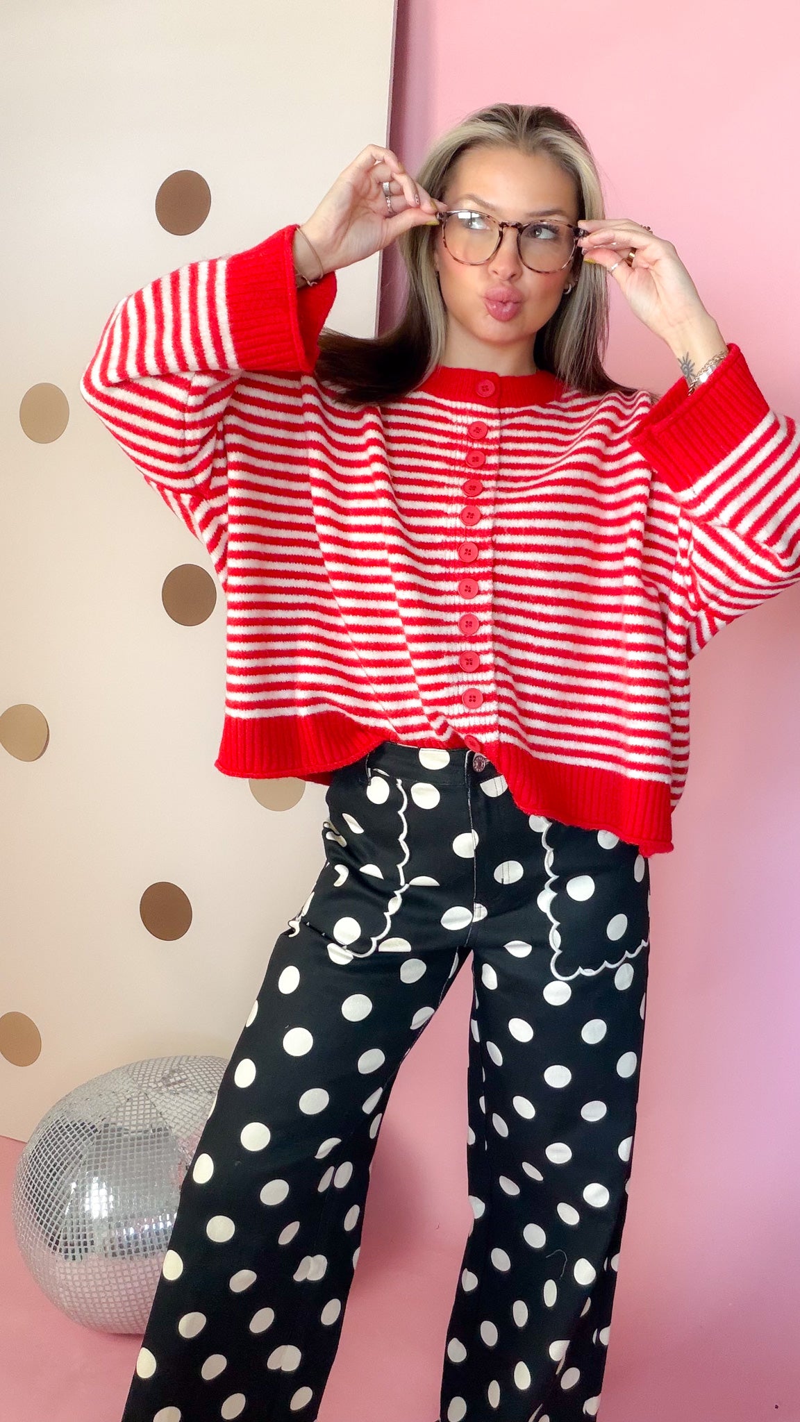 Red and ivory striped sweater with boxy silhouette and wide red cuffs, shown with model adjusting glasses.