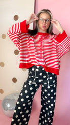 Red and ivory striped sweater with boxy silhouette and wide red cuffs, shown with model adjusting glasses.