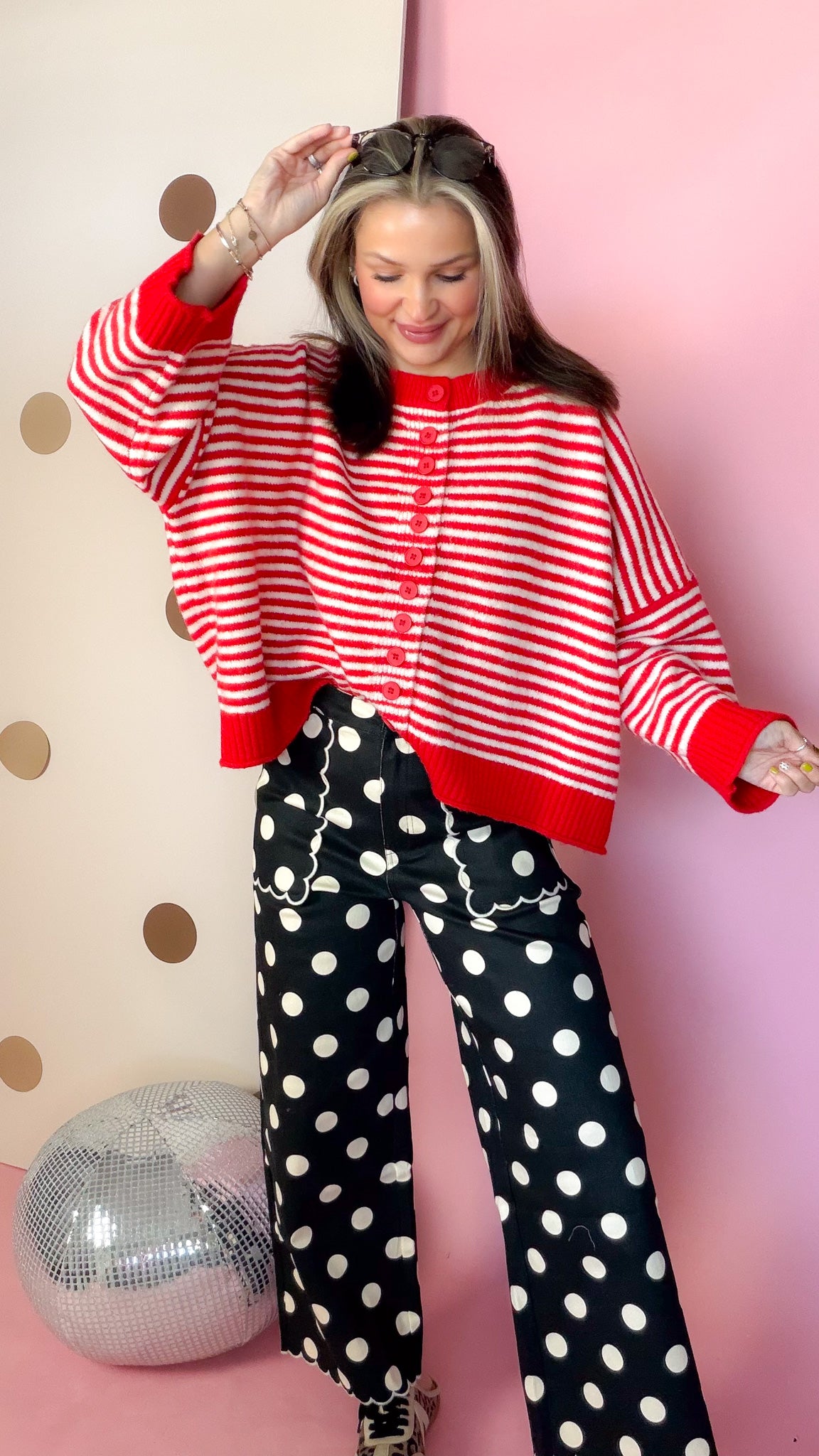 Black polka dot wide leg pants with scalloped pocket trim, styled with a red striped cardigan and sneakers.