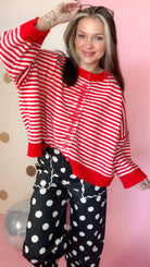 Close front view of red and ivory striped sweater showing red buttons, round neckline, and solid red hem.