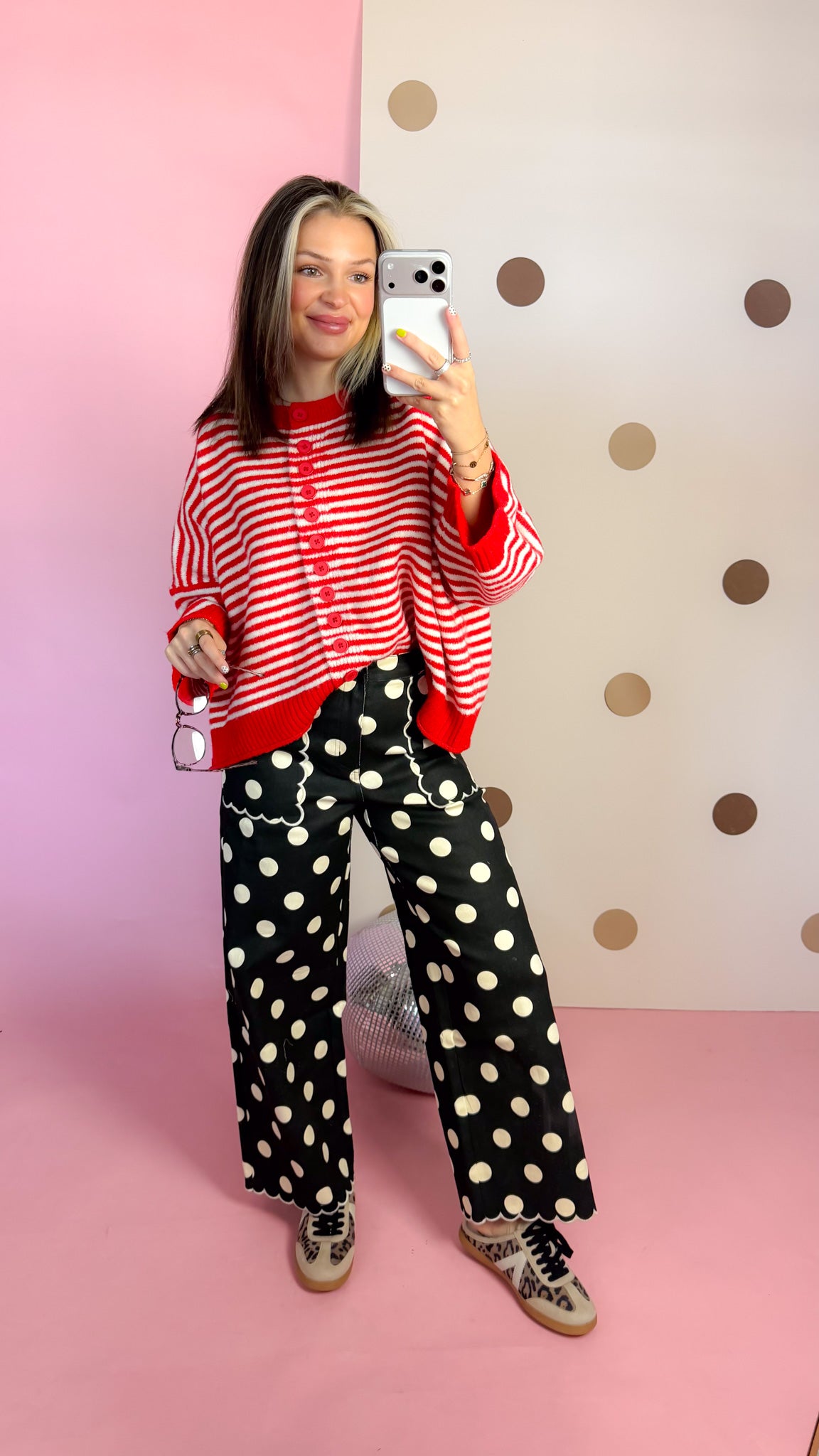 Full-length mirror view of black polka dot wide leg pants paired with a red striped cardigan and printed sneakers.