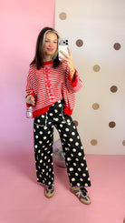 Full-length mirror view of black polka dot wide leg pants paired with a red striped cardigan and printed sneakers.