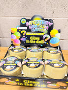 Full display of glow-in-the-dark dumpling squishy packages in yellow steamer-style containers on a wooden tabletop.