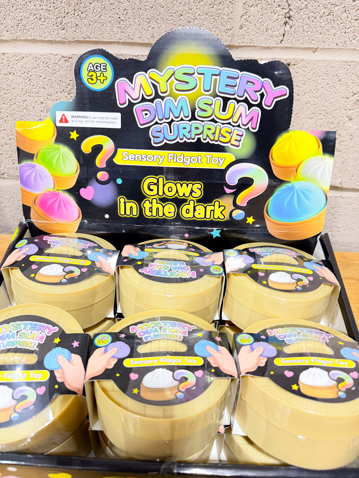 Close-up of Mystery Dim Sum Surprise squishy display with round yellow containers and Glows in the Dark signage.