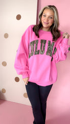 Front view of a model wearing the bubblegum pink Lulu Mac Bottomland camo sweatshirt with black pants.