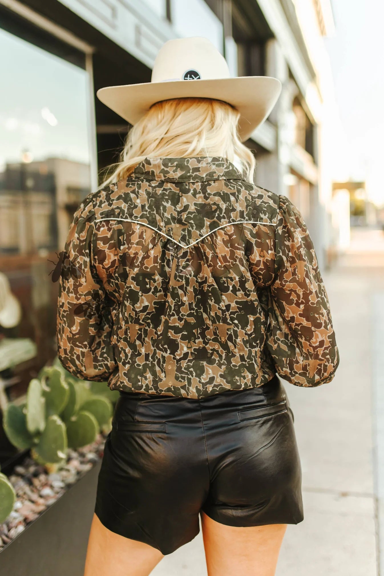 Person wearing a camouflage jacket and black shorts with a blurred urban background
