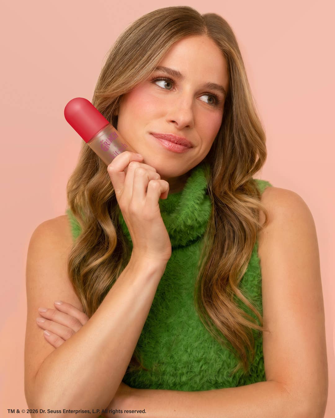 The Grinch x Kitsch Cherry Cheer hair perfume held to the cheek by a model in green