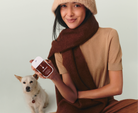 Model in a knit hat and scarf holding Touchland Salted Caramel next to a small dog