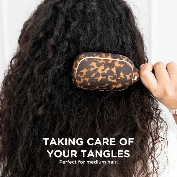 Woman brushing long curly hair with the Teleties tortoise Detangler Brush, with text overlay