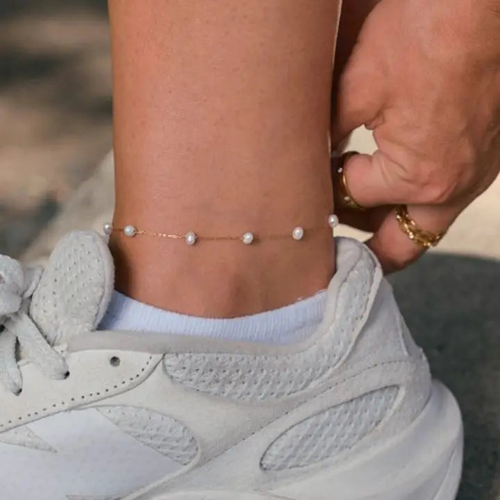 Camille gold-tone pearl anklet worn around an ankle above a white sock and white sneaker.