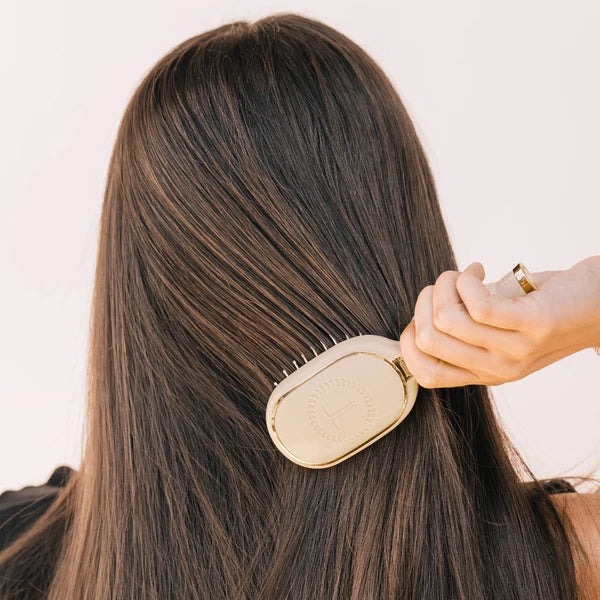 Woman brushing long dark hair with the Teleties Mini Detangler Brush in tan
