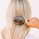 Woman brushing long blonde hair with the Teleties Mini Detangler Brush in tortoise