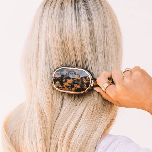 Woman brushing long blonde hair with the Teleties Mini Detangler Brush in tortoise
