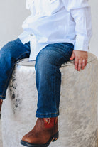 A toddler wearing a white shirt and blue slim straight jeans, sitting on a textured surface.